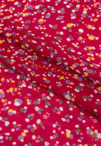 Tissu rouge à motif de pois éparpillés de couleurs variées, y compris le jaune, le violet et le blanc, avec une texture douce et lisse.