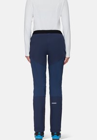 Marineblauwe skibroek met een nauwsluitend ontwerp, gestructureerde stof en een zwarte tailleband. Bevat merkspecificatie op het onderbeen en versteviging bij de enkels.