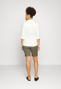 Camisa branca de manga longa e calções verdes-oliva, vista de trás. A camisa está abotoada com as mangas arredondadas; os calções têm comprimento hasta ao joelho com bainhas.