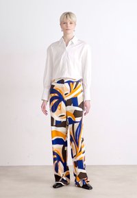 Camisa blanca de manga larga combinada con pantalones de pierna ancha que presentan un patrón abstracto colorido en azul, naranja y marrón. Textura de tela suave.