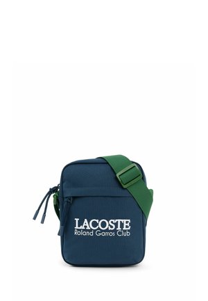 Kleine marineblauwe Lacoste Roland Garros Club schoudertas met een brede verstelbare groene band en een voorvak met ritssluiting.