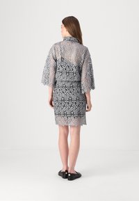 Blondekjole og matchende cover-up; sølvgrå farge; flagrende ermer; intrikat blomstermønster; kne-lengde skjørt; sømløst design.