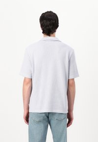 Polo a maniche corte in tessuto grigio chiaro testurizzato con colletto, caratterizzato da un motivo diagonale e dettagli con spacchi laterali.