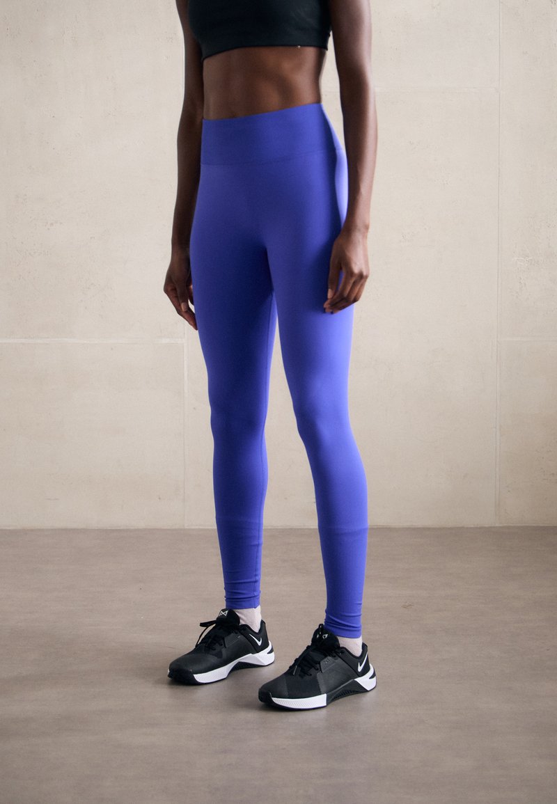 Lila träningsleggings gjorda av stretchy tyg, med hög midja och en slät yta, parat med svarta träningsskor.
