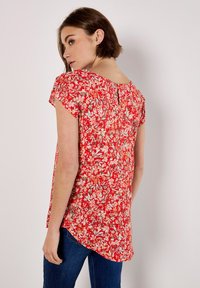 Blusa roja con flores, de mangas cortas, con escote redondo y un detalle en forma de ojo de cerradura en la parte posterior. Tejido ligero con un corte holgado y dobladillo curvado.