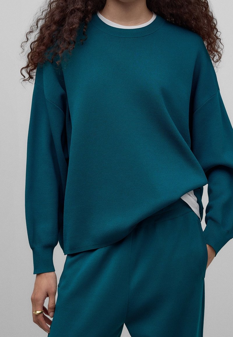 Turkusowy, oversize'owy sweatshirt z miękkiego, teksturowanego materiału z okrągłym dekoltem, w zestawie z dopasowanymi spodniami typu tapered. Prosty design bez wzorów.