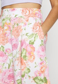 Pantalones florales en tela blanca con grandes peonías rosas y naranjas con hojas verdes. Diseñados con bolsillos laterales y detalles plisados.