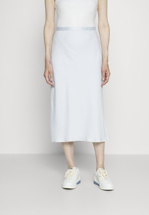 Jupe midi bleu clair en tissu lisse avec une taille ajustée et une ceinture en satin, associée à des baskets blanches.