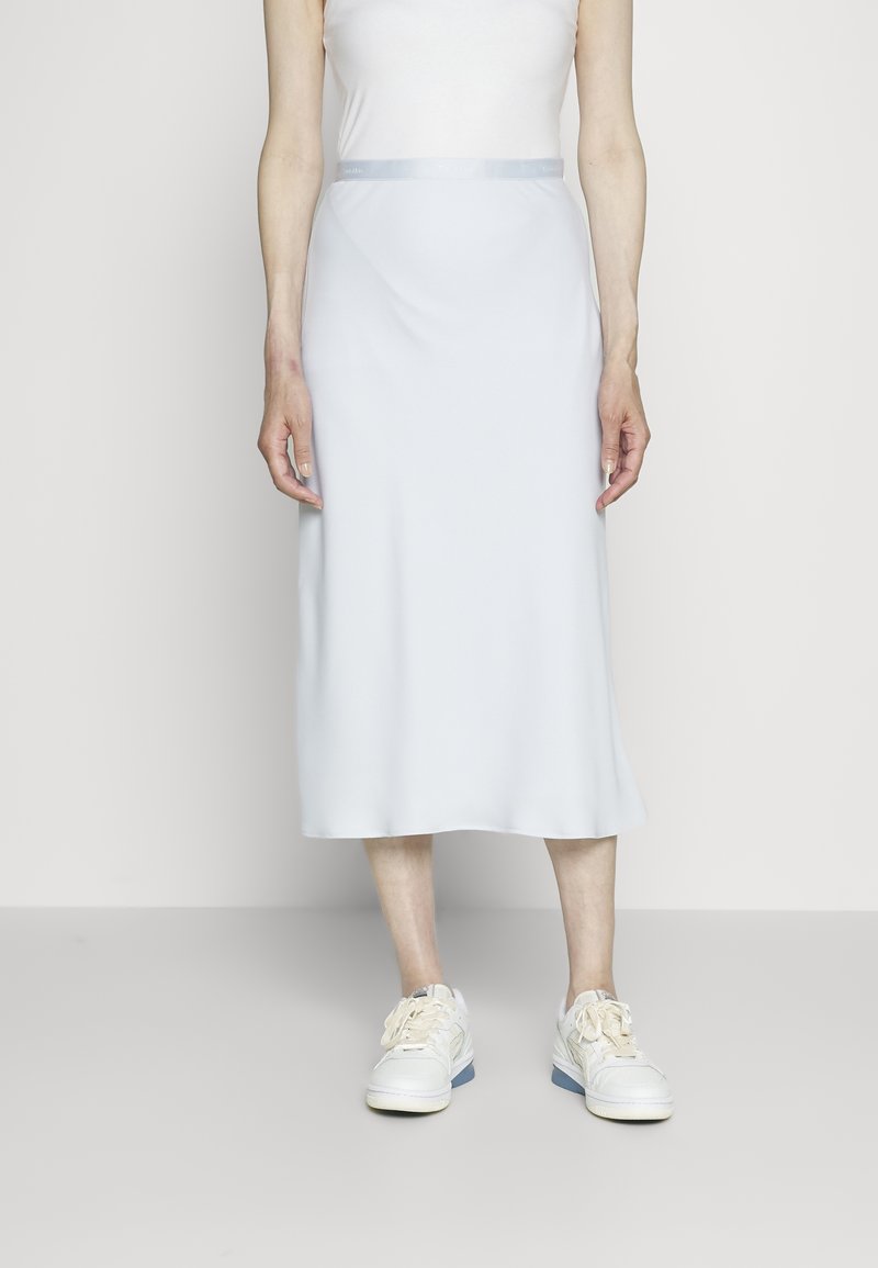 Světle modrá midi sukně vyrobená z hladkého materiálu s těsným pasem a saténovým pasem, spárovaná s bílými teniskami.