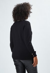 Maglione nero a maniche lunghe, con dettagli di bottoni dorati ai polsini e scollatura rotonda. Tessuto morbido e forma aderente.