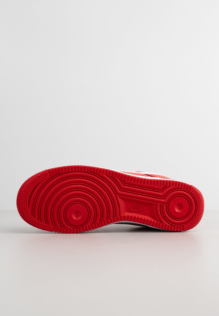 Semelle de sneaker en caoutchouc rouge avec un motif de bande de roulement circulaire et des bosses surélevées. Présente le logo Nike en relief subtil près du talon.