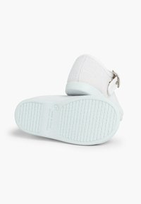 Sandale din material textil alb, cu un bretele texturate și cataramă argintie, având o talpă din cauciuc albastru deschis, care prezintă un profil cu model.