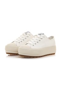 Zapatillas de lona blancas con una suela de goma elevada y una suela de goma marrón. Presentan puntera redonda, diseño de cordones y ojales plateados para los cordones.