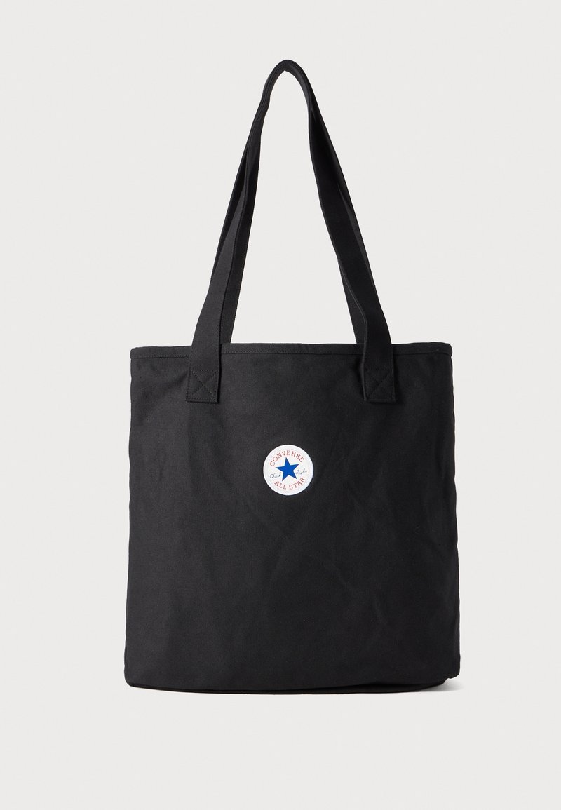 Sac fourre-tout en toile noire avec deux poignées robustes, ornée d'un patch circulaire avec une étoile bleue et le texte "Converse All Star".