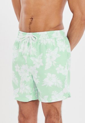 Shorts de bain vert menthe avec motif floral blanc, taille élastique, cordon de serrage et poches latérales. Tissu léger et coupe décontractée.