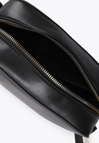 Borsa in pelle nera parzialmente aperta, che rivela un interno con cerniera. La cerniera è dorata, evidenziando il design elegante della borsa.
