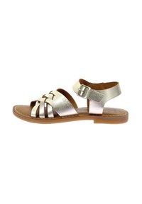 Sandal de cuero metálico dorado con correas frontales trenzadas, correa ajustable en el tobillo con hebilla y suela plana de goma marrón.