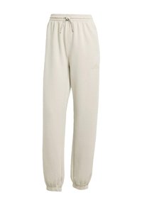Pantalones de chándal beige claro con cintura elástica y cordón decorativo. Tobillos con puños y un sutil detalle del logo en la cadera. Textura de tela suave.