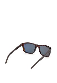 Lunettes de soleil à monture écaille avec des verres bleu foncé et des branches noires, reposant ouvertes sur une surface blanche.