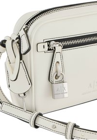 Borsa a tracolla sintetica bianca con accenti neri, chiusura con zip, hardware argentato e dettagli con logo. Caratterizzata da tracolla regolabile e finitura testurizzata.