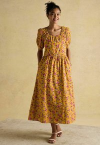 Kollane lilleline maksikleit puffvarrukatega, elastse vöökoht ja küljetaskud. Peal on roosa ja sinine lillemuster tekstureeritud kangal.