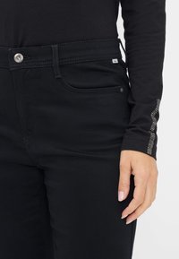 Zwarte jeans met een slim fit ontwerp, met een glanzende klinknagelknop, subtiele stiksels op de zakken en een gestructureerd accent langs de zijnaad.