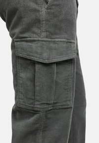 Grå corduroy cargo bukser med sidelomme med klaff og ribbet tekstur. Sømmenes syninger gir holdbarhet til designet.