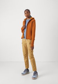 Orange zip-up hoodie, blå t-shirt, beige cargo-byxor och grå trail-skor. Utstyrslen har en avslappnad passform och funktionella fickor.