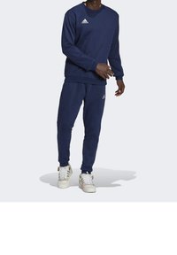 Felpa blu navy e pantaloni jogger realizzati in morbido materiale, con scollo rotondo e logo bianco Adidas sul petto e sulla gamba del pantalone.