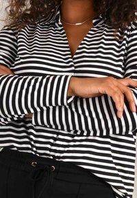 Schwarz-weiße gestreifte Langarmbluse mit Kragen, entspannter Schnitt und Knopfdetail am Ausschnitt. Strukturierter Stoff, minimalistisches Design.