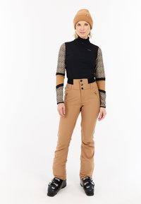 Zwart en beige lange mouwen met rits bovenstuk met leopardprint armen, gecombineerd met beige sneeuwbroeken en zwarte skibotten. Gezellige gebreide muts.