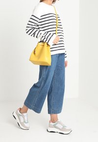 Maglia a maniche lunghe a righe in bianco e blu navy; pantaloni in denim a gamba larga blu; borsa a secchiello gialla; sneakers grigie e bianche con dettagli verdi.