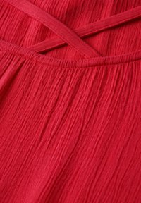 Tessuto rosso testurizzato con un design a tracolla incrociato, caratterizzato da una superficie morbida e stropicciata e dettagli arricciati sulla cucitura.