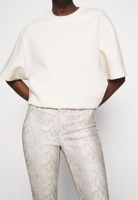 White oversized short-sleeve sweater paired with light-colored snake-patterned pants featuring a smooth texture and slim fit.