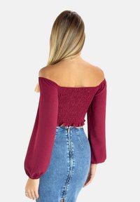 Burgunderfarvet off-shoulder top med smocket bodice, flæsekanter og lange ballonærmer, parret med en lysvasket denim-nederdel med slid foran.