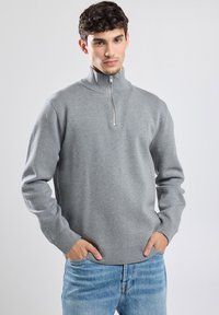Gray zip-neck sweatshirt made of soft fabric, featuring long sleeves, ribbed hem, and a metal zipper, paired with light blue jeans.