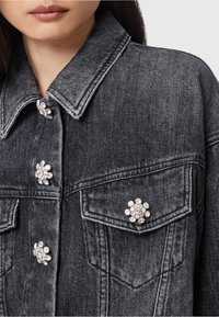 Chaqueta de mezclilla negra con cuello clásico, adornada con botones de strass en forma de flor decorativos y dos bolsillos frontales.