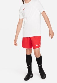 Bílý tričko Nike s červeným logem, červené šortky s bílým lemováním, černé podkolenky a černé kopačky. Jednoduchý sportovní design.