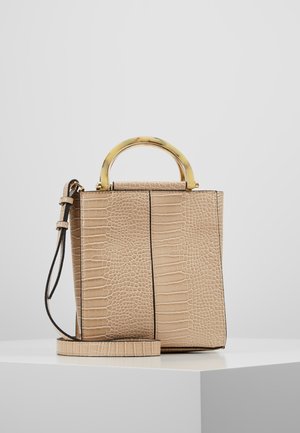 Beige håndtaske med krokodilletekstur, gyldigt buet øverste håndtag i guld og matchende justerbar skulderrem på hvid piedestal.