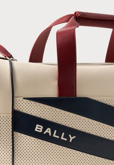 Μπεζ δερμάτινη τσάντα με τρύπες και ναυτικό διαγώνιο σχέδιο, κόκκινες δερμάτινες λαβές και το "BALLY" τυπωμένο στη μπροστινή λωρίδα.