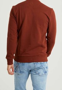 Brun sweatshirt med långa ärmar i texturerat tyg, med ribbad midjeresår och muddar, kombinerad med ljusblå slitna jeans.