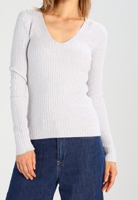 Haut gris clair côtelé à manches longues avec un col en V et une coupe ajustée, associé à un jean en denim bleu.