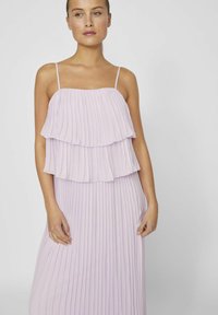 Robe lilas plissée avec des volants superposés au niveau du corsage, fines bretelles ajustables et jupe fluide qui descend jusqu'au sol.