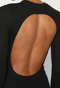 Schwarzes, geripptes Strickkleid mit einem großen, ovalen Ausschnitt auf dem Rücken, der eine glatte, nackte Hauttextur betont. Enganliegendes Design.