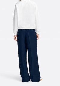 Sweatshirt bianco a vita alta con polsini a costine, abbinato a pantaloni larghi blu navy con pieghe e una superficie liscia.