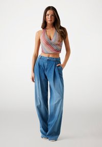 Multicolor halter crop top with a wave pattern. Paired with loose-fitting, light blue high-waisted denim pants with pleats.