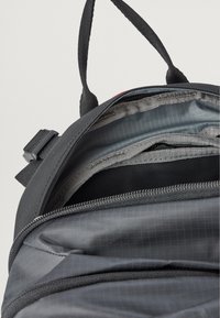 Zaino nero realizzato in tessuto testurizzato, con più scomparti e cerniere, caratterizzato da una fodera grigia con un sottile motivo a griglia. Spallacci regolabili.