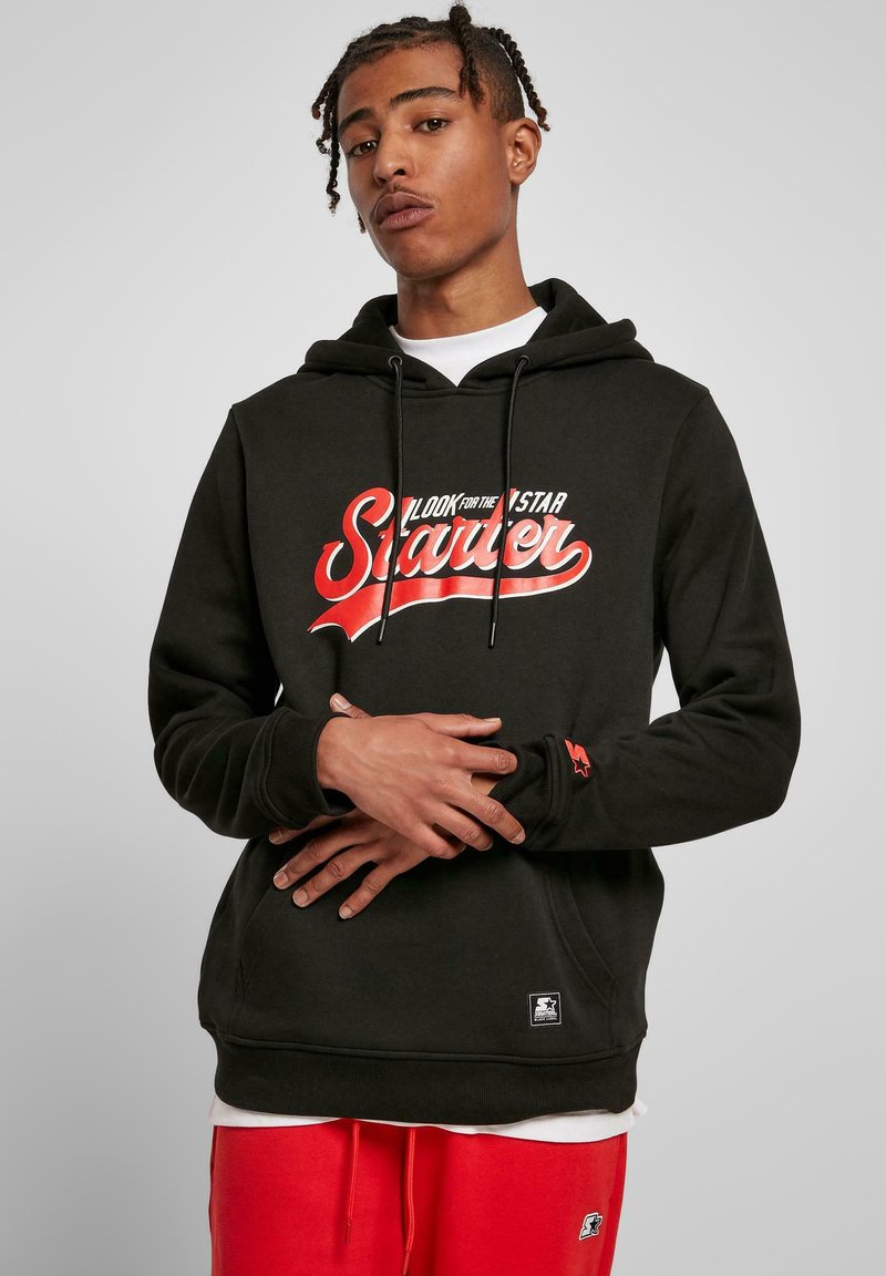 Sudadera con capucha negra que presenta un logo en script rojo, cordones, bolsillo frontal y tela texturizada. Acentuada con un logo de estrella roja en la manga.