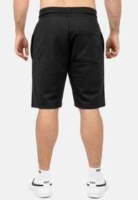 Shorts neri in cotone con tasche laterali e una tasca posteriore. Caratterizzati da una vestibilità rilassata e una cintura elasticizzata. Indossati con sneaker bianche.