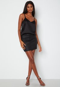 Camisole in raso nero con spalline sottili, abbinato a una mini gonna in denim nero aderente, completato da sandali neri con cinturini.